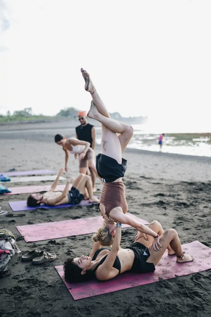 Yoga students practicing partner yoga poses on a beach during a group session.